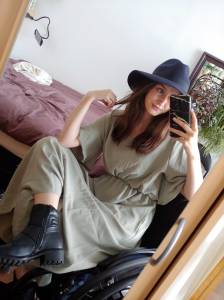 Foto van Birgit, een jonge, witte vrouw met lang lichtbruin haar, poserend in hippe kleren en een hoed vóór haar bed